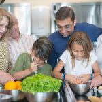 Family of various ages gathers in kitchen to cook meal together, showcasing culinary togetherness.